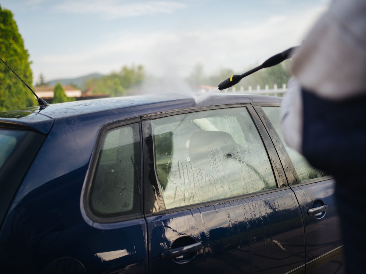 Rinsing a car with a pressure washer in a residential driveway
